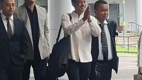 Nadiem tampak mengenakan kemeja berwarna putih gading, celana panjang berwarna hitam, dan membawa tas jinjing berwarna hitam.
