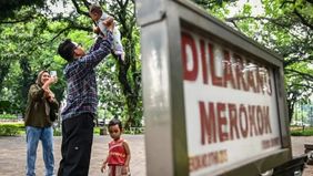 Warga bermain bersama anaknya di samping papan informasi larangan merokok di Taman Suropati, Jakarta, Rabu, 30 Juli 2025.