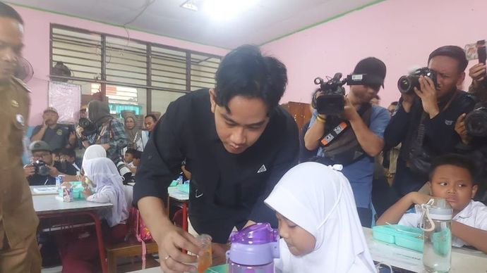 Wakil Presiden Terpilih Gibran Rakabuming Raka membantu seorang siswa menuangkan menu makanan saat memantau uji coba program makan bergizi gratis (MBG) di SDN 4 Tangerang Senin (5/8/2024). 