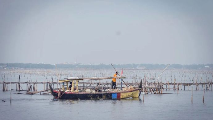 Nelayan menggunakan perahu melintas di dekat pagar laut di Pantai Anom, Desa Kohod, Kabupaten Tangerang, Banten, Jumat (24/1/2025)