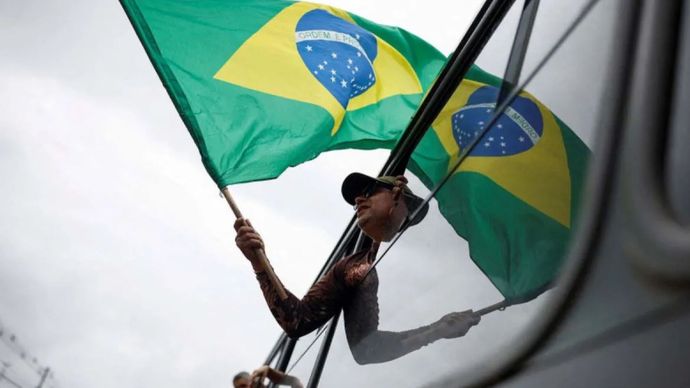 Seorang pria memegang bendera Brasil dari jendela bus saat dia ditahan setelah kamp yang didirikan oleh pendukung mantan Presiden Brasil Jair Bolsonaro dibubarkan di Brasilia, Brasil, (9/1/2023).