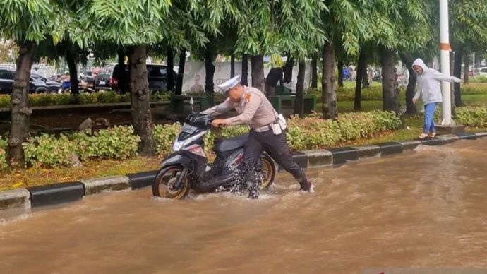 Petugas kepolisian mendorong sepeda motor milik seorang wanita yang mogok akibat kemasukan air banjir di Jalan Pesanggrahan, Kembangan Selatan, Jakarta Barat, Selasa 3 Maret 2025