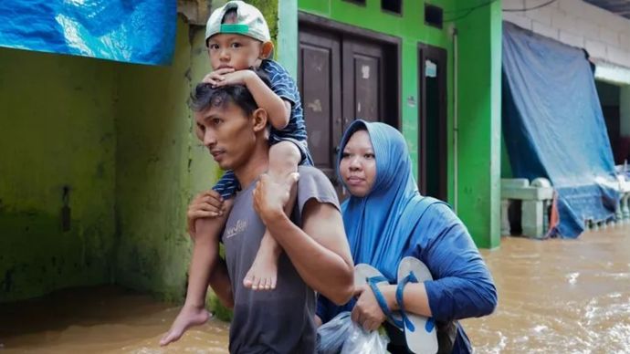 Warga mengendong anaknya saat melintasi banjir di Kebon Pala, Jakarta, Selasa 4 Maret 2025.