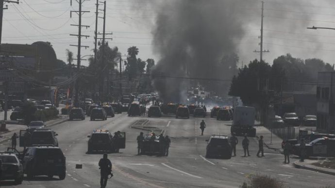 Asap tebal membubung saat pengunjuk rasa bentrok sengit dengan deputi sheriff Los Angeles di Paramount, Los Angeles County, California, pada 7 Juni 2025. Sabtu itu, sejumlah orang ditangkap setelah aksi protes memanas selama dua hari berturut-turut m