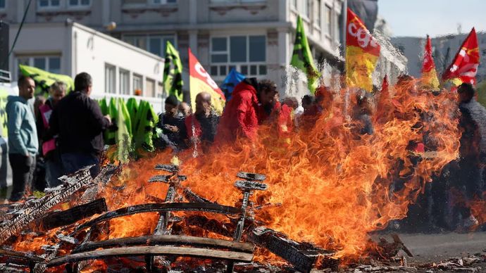 Pekerja kereta api SNCF Prancis melakukan aksi mogok, memegang bendera serikat pekerja CGT dan Sud Rail Prancis, berkumpul di dekat palet kayu yang terbakar di stasiun kereta api Gare de Lyon sebagai bagian dari 