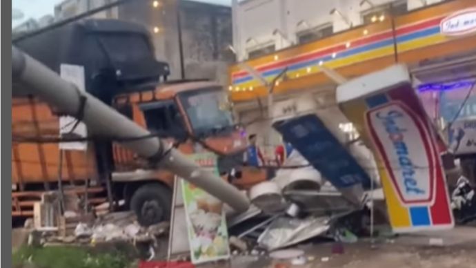 Dalam video yang viral di media sosial TikTok, terlihat truk berwarna oranye dengan muatan besar melintang di badan jalan, sementara bagian depan kendaraan menghantam bangunan hingga rusak parah.
