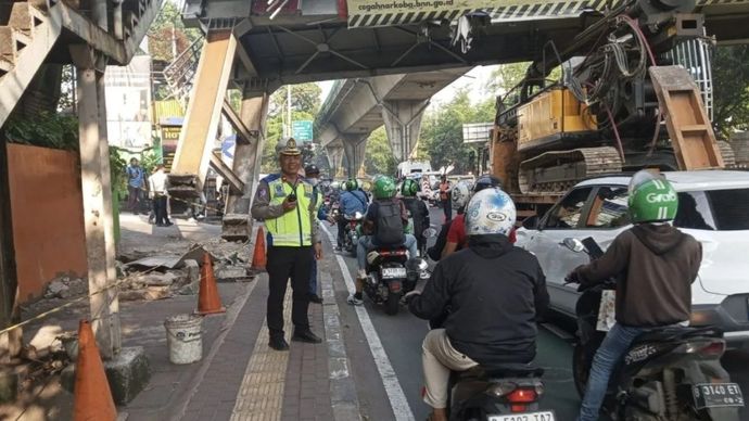 Petugas Ditlantas Polda Metro Jaya sedang melakukan pengaturan di lokasi tempat kejadian truk yang membawa muatan alat berat hingga tersangkut di Jembatan Penyeberangan Orang (JPO) di kawasan Mampang Prapatan, Jakarta Selatan, Selasa, 14 Juli 2026.