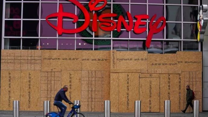 Seorang pria berjalan melewati toko Disney yang ditutup dengan papan di Times Square, New York, Amerika Serikat