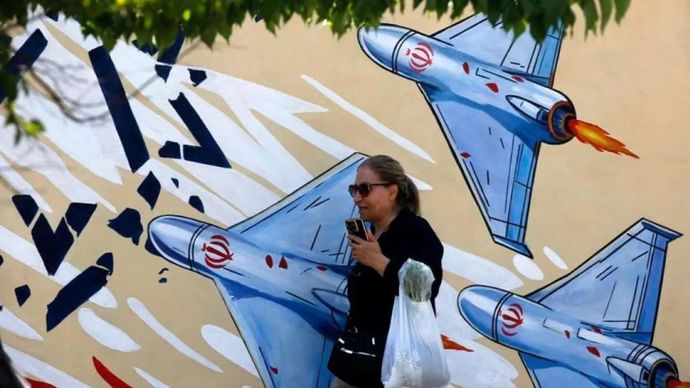 Seorang perempuan berjalan di jalanan dengan latar belakang tembok bermuralkan pesawat tempur Iran di Teheran, Iran, pada 8 Juni 2026