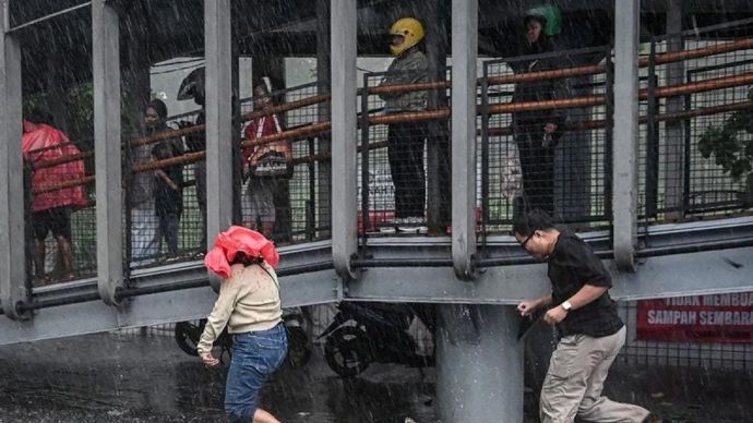 Ilustrasi - Warga berlari menerobos hujan lebat di pedestrian Jalan Sudirman, Jakarta