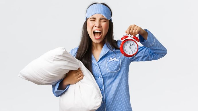 Ilustrasi - seseorang merasa kesal saat alarm berbunyi di pagi hari karena kurang tidur.