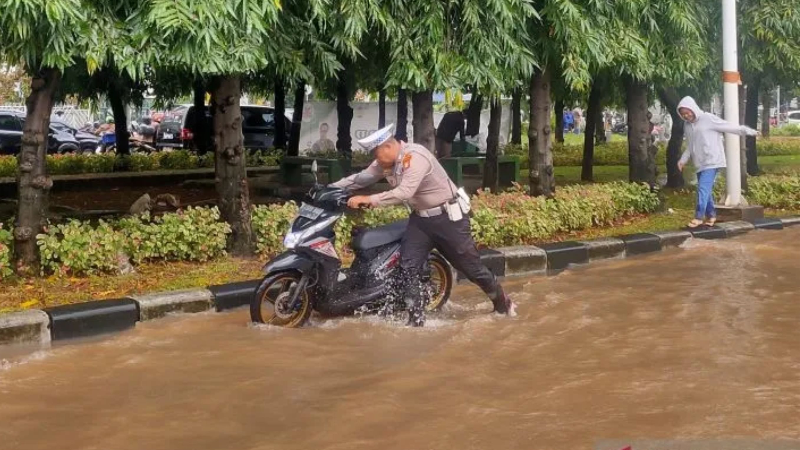 Petugas kepolisian mendorong sepeda motor milik seorang wanita yang mogok akibat kemasukan air banjir di Jalan Pesanggrahan, Kembangan Selatan, Jakarta Barat, Selasa 3 Maret 2025 <b>(Antara)</b>