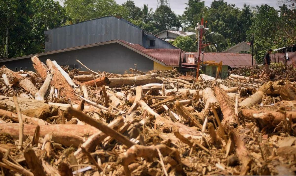 Warga melintas di antara tumpukan gelondongan kayu di permukiman di Tabiang Bandang Gadang, Nanggalo, Padang, Sumatera Barat, Selasa (9/12/2025). Gelondongan kayu yang terbawa banjir bandang sejak dua pekan lalu masih tersangkut di wilayah itu. ANTAR <b>(Antara)</b>