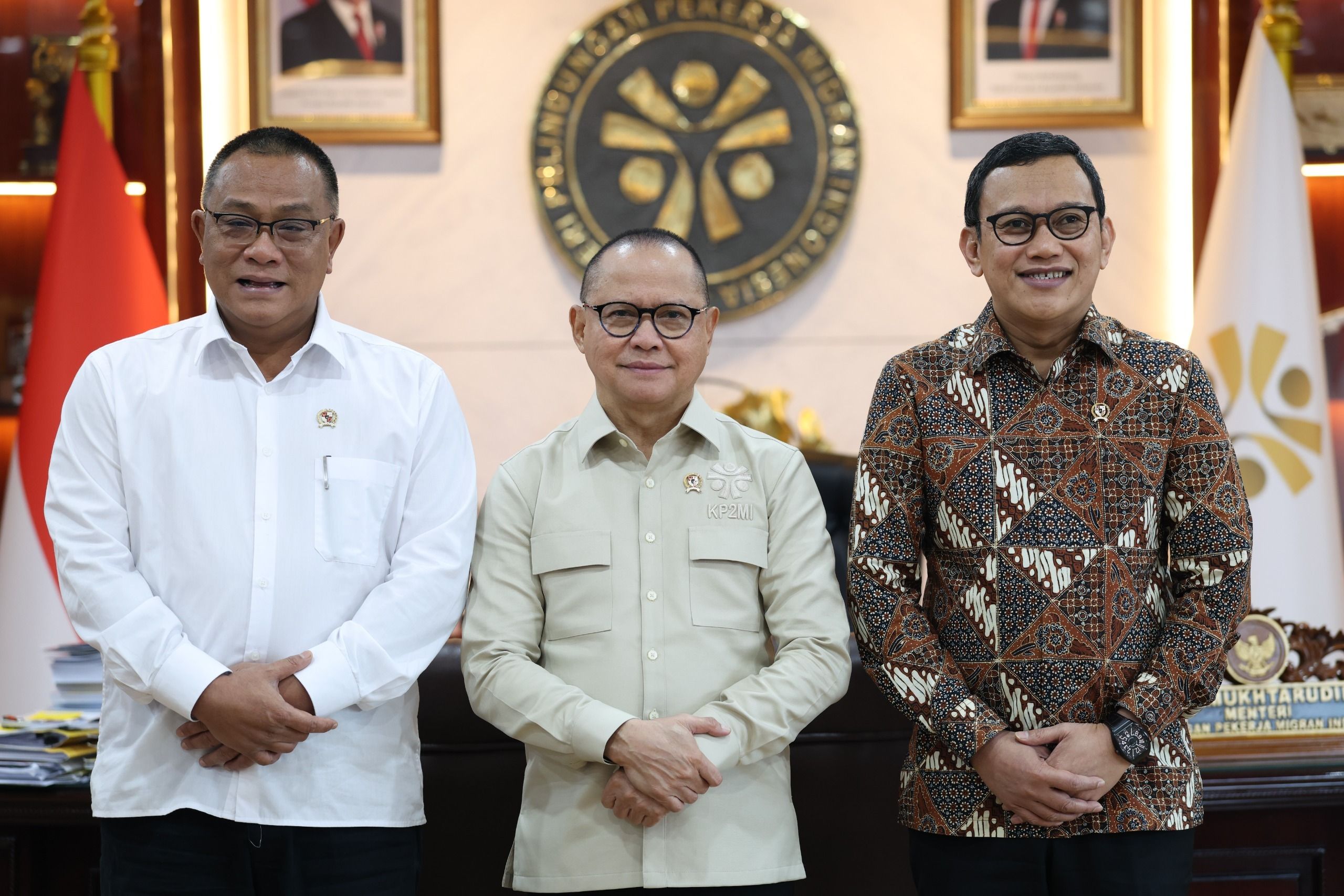 Foto bersama jajaran kepemimpinan Kementerian P2MI. Kiri: Deputi Bidang Pelindungan; Tengah: Menteri P2MI Mukhtarudin; Kanan: Sekretaris Kementerian. Kehadiran logo resmi kementerian di latar belakang mempertegas formalitas momen.