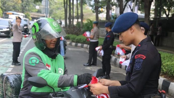 Seorang personel Brimob Polda Metro Jaya membagikan bendera merah putih kepada sejumlah pengendara sepeda motor yang melintas di kawasan Jakarta Pusat, Senin 4 Agustus 2025. ANTARA/HO-Humas Polda Metro Jaya