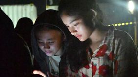 Malam hari di Kecamatan Rantau, Aceh Tamiang, berubah menjadi ruang berkumpul tak biasa. Di tanah berpasir, di bawah cahaya seadanya, warga dari berbagai usia duduk berkelompok sambil menatap layar ponsel mereka. Ada yang mengisi daya telepon genggam