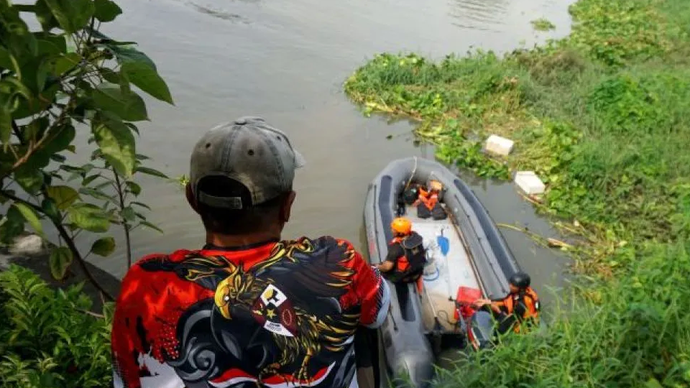 Seorang warga melihat petugas Tim SAR gabungan melakukan pencarian balita hanyut terseret arus di Kali Makmur kawasan perumahan Royal Residen Surabaya, Kamis (26/12/2024).