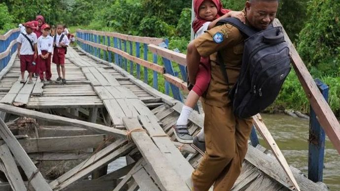 seorang guru menggendong siswa SD Negeri 1 Alaaha saat menyeberangi jembatan rusak di Desa Alaaha, Kecamatan Ueesai, Kolaka Timur, Sulawesi Tenggara,  Jumat 15 November 2024.